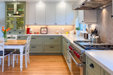 Large country u-shaped eat-in kitchen in San Francisco with a farmhouse sink, shaker cabinets, green cabinets, quartz benchtops, grey splashback, porcelain splashback, stainless steel appliances, medium hardwood floors and white benchtop.
