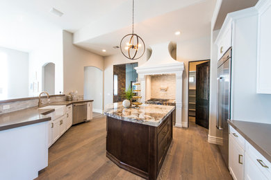 Mid-sized contemporary u-shaped open plan kitchen in Phoenix with a farmhouse sink, shaker cabinets, white cabinets, stainless steel appliances, medium hardwood floors, with island, brown floor, quartz benchtops, grey splashback and grey benchtop.
