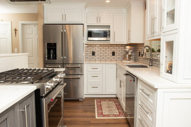 ポートランド(メイン)にあるお手頃価格の広いトランジショナルスタイルのおしゃれなキッチン (アンダーカウンターシンク、インセット扉のキャビネット、白いキャビネット、クオーツストーンカウンター、白いキッチンパネル、サブウェイタイルのキッチンパネル、シルバーの調理設備、濃色無垢フローリング、茶色い床、白いキッチンカウンター) の写真