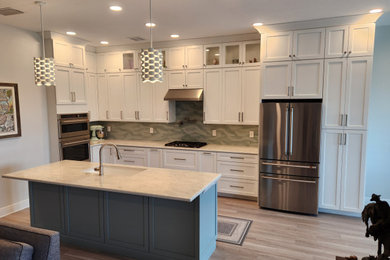 Mid-sized beach style l-shaped laminate floor and gray floor open concept kitchen photo in Tampa with an undermount sink, shaker cabinets, white cabinets, quartz countertops, multicolored backsplash, glass tile backsplash, stainless steel appliances, an island and multicolored countertops