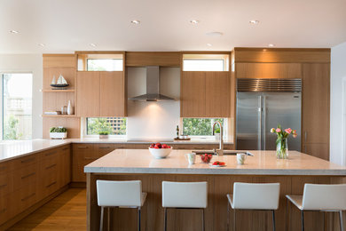 Photo of a contemporary l-shaped kitchen in Other with an undermount sink, flat-panel cabinets, medium wood cabinets, window splashback, stainless steel appliances, medium hardwood floors, with island, brown floor and quartz benchtops.