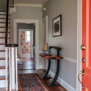 Eklektisk inredning av en foajé, med grå väggar, mellanmörkt trägolv, en enkeldörr, en orange dörr och brunt golv