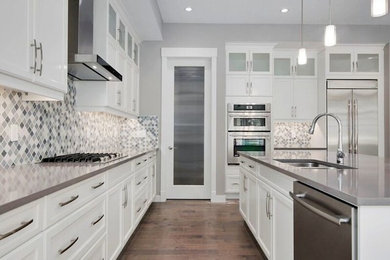Eat-in kitchen - large l-shaped medium tone wood floor eat-in kitchen idea in Calgary with a double-bowl sink, shaker cabinets, white cabinets, solid surface countertops, gray backsplash, mosaic tile backsplash, stainless steel appliances and an island