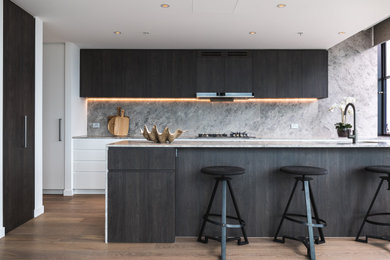 Design ideas for a contemporary galley kitchen in Sydney with flat-panel cabinets, black cabinets, grey splashback, medium hardwood floors, with island, brown floor and grey benchtop.