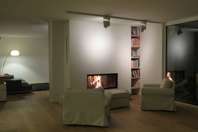 Großes, Offenes Modernes Wohnzimmer mit weißer Wandfarbe, hellem Holzboden, Tunnelkamin, verputzter Kaminumrandung und beigem Boden in Köln