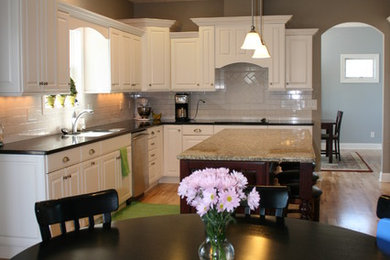 Mid-sized elegant light wood floor and beige floor eat-in kitchen photo in Omaha with an undermount sink, raised-panel cabinets, white cabinets, granite countertops, white backsplash, subway tile backsplash, stainless steel appliances and an island