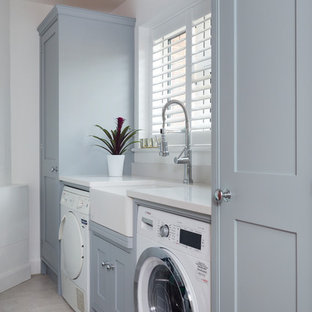 Design ideas for a small classic single-wall laundry cupboard in Kent with a belfast sink, shaker cabinets, grey cabinets, quartz worktops, white walls, ceramic flooring, a side by side washer and dryer and beige floors.