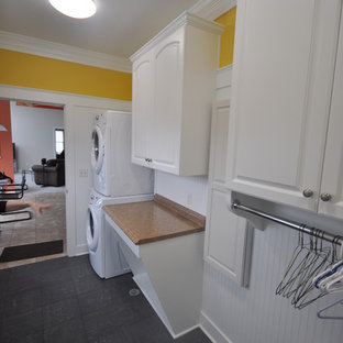 他の地域の小さいトラディショナルスタイルのおしゃれな家事室 (レイズドパネル扉のキャビネット、白いキャビネット、ラミネートカウンター、黄色い壁、セラミックタイルの床、上下配置の洗濯機・乾燥機) の写真