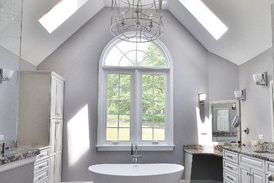 Design ideas for a large transitional master bathroom in Philadelphia with raised-panel cabinets, granite benchtops, a freestanding tub, a one-piece toilet, porcelain tile, grey walls, porcelain floors, white cabinets, a corner shower, beige tile, an undermount sink, grey floor and a hinged shower door.