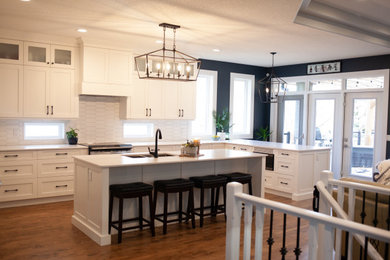 Eat-in kitchen - large transitional u-shaped medium tone wood floor, orange floor and coffered ceiling eat-in kitchen idea in Edmonton with an undermount sink, shaker cabinets, white cabinets, quartz countertops, white backsplash, ceramic backsplash, stainless steel appliances, two islands and white countertops