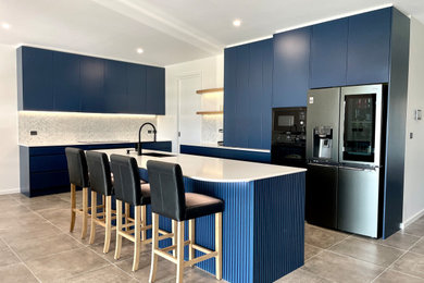 Design ideas for a large modern l-shaped open plan kitchen in Sydney with a drop-in sink, flat-panel cabinets, blue cabinets, quartz benchtops, grey splashback, marble splashback, black appliances, ceramic floors, with island, grey floor and white benchtop.