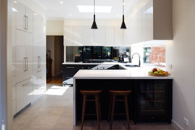 Photo of a mid-sized contemporary u-shaped eat-in kitchen in Melbourne with a double-bowl sink, recessed-panel cabinets, black cabinets, quartz benchtops, black splashback, mirror splashback, black appliances, a peninsula, beige floor and white benchtop.