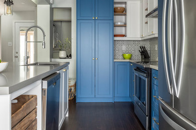 This is an example of a kitchen in Toronto with blue cabinets, grey splashback, stainless steel appliances, with island, brown floor and grey benchtop.