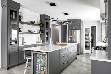 Example of a mid-sized trendy galley vinyl floor and gray floor kitchen design in Other with a double-bowl sink, glass-front cabinets, gray cabinets, quartz countertops, white backsplash, marble backsplash, stainless steel appliances, an island and white countertops