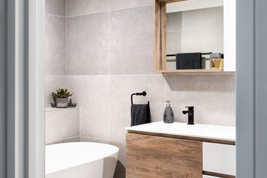 Mid-sized contemporary master bathroom in Wollongong with beaded inset cabinets, medium wood cabinets, a freestanding tub, a corner shower, a one-piece toilet, gray tile, limestone, grey walls, ceramic floors, an integrated sink, engineered quartz benchtops, grey floor, a hinged shower door and white benchtops.