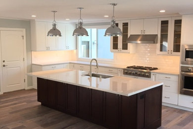 Example of a large trendy l-shaped dark wood floor eat-in kitchen design in San Francisco with a drop-in sink, shaker cabinets, white cabinets, laminate countertops, white backsplash, cement tile backsplash, stainless steel appliances and an island
