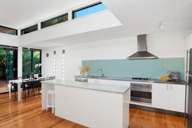 This is an example of a modern galley open plan kitchen in Sydney with flat-panel cabinets, white cabinets, quartz benchtops and with island.