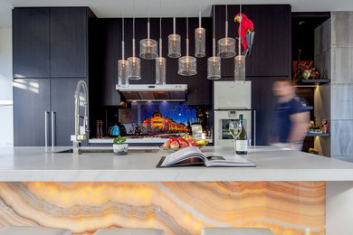 Photo of a mid-sized contemporary single-wall open plan kitchen in Melbourne with a double-bowl sink, flat-panel cabinets, dark wood cabinets, marble benchtops, multi-coloured splashback, glass sheet splashback, white appliances, dark hardwood floors, with island, brown floor and white benchtop.