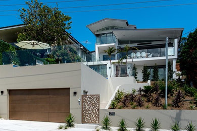 This is an example of a modern three-storey stucco beige house exterior in Sydney with a shed roof and a metal roof.