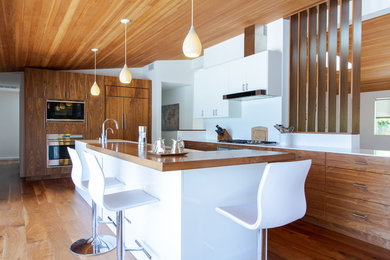 Inspiration for a 1960s medium tone wood floor kitchen remodel in Los Angeles with flat-panel cabinets, medium tone wood cabinets, white backsplash, paneled appliances, an island and white countertops