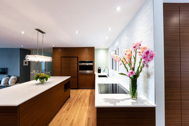 Example of a mid-sized trendy l-shaped light wood floor and brown floor open concept kitchen design in Toronto with a double-bowl sink, flat-panel cabinets, medium tone wood cabinets, quartz countertops, white backsplash, glass tile backsplash, stainless steel appliances, an island and white countertops