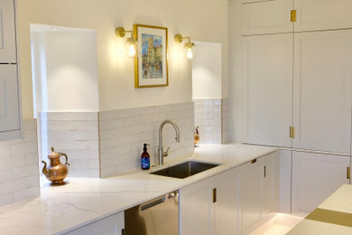 Design ideas for a large modern cream and black kitchen in Gloucestershire with a built-in sink, shaker cabinets, quartz worktops, white splashback, metro tiled splashback, integrated appliances, limestone flooring, an island, beige floors, multicoloured worktops, exposed beams and feature lighting.