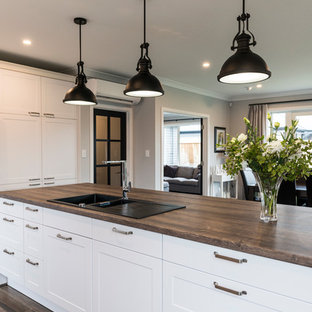 Large transitional kitchen pantry remodeling - Large transitional l-shaped vinyl floor and brown floor kitchen pantry photo in Christchurch with a farmhouse sink, shaker cabinets, white cabinets, laminate countertops, black backsplash, glass sheet backsplash, stainless steel appliances and an island