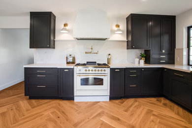 Huge minimalist l-shaped medium tone wood floor eat-in kitchen photo in Los Angeles with a farmhouse sink, shaker cabinets, black cabinets, white backsplash, white appliances, no island and white countertops