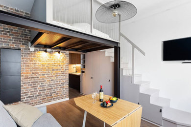 Cette image montre un petit salon mansardé ou avec mezzanine urbain avec un mur blanc, un sol en contreplaqué, aucune cheminée, un téléviseur encastré et un escalier.
