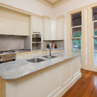 Mid-sized victorian kitchen pantry appliance - Example of a mid-sized ornate galley medium tone wood floor kitchen pantry design in Gold Coast - Tweed with an undermount sink, recessed-panel cabinets, marble countertops, beige backsplash, ceramic backsplash, stainless steel appliances, an island and beige cabinets
