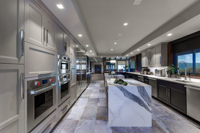 Example of a large transitional porcelain tile, gray floor and tray ceiling kitchen design in Other with a single-bowl sink, recessed-panel cabinets, gray cabinets, quartz countertops, white backsplash, glass sheet backsplash, stainless steel appliances, two islands and gray countertops