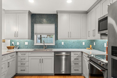 Inspiration for a mid-sized modern u-shaped medium tone wood floor kitchen pantry remodel in Tampa with an undermount sink, shaker cabinets, gray cabinets, quartz countertops, blue backsplash, glass tile backsplash, stainless steel appliances, a peninsula and gray countertops