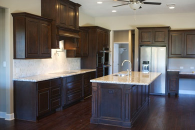 Inspiration for a large timeless l-shaped dark wood floor and brown floor kitchen remodel in Houston with a single-bowl sink, raised-panel cabinets, dark wood cabinets, granite countertops, white backsplash, ceramic backsplash, stainless steel appliances and an island