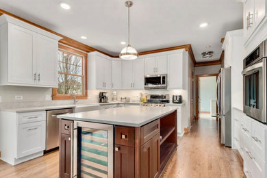 Example of a large country u-shaped light wood floor and gray floor eat-in kitchen design in Chicago with a farmhouse sink, shaker cabinets, dark wood cabinets, quartz countertops, gray backsplash, quartz backsplash, stainless steel appliances, an island and white countertops