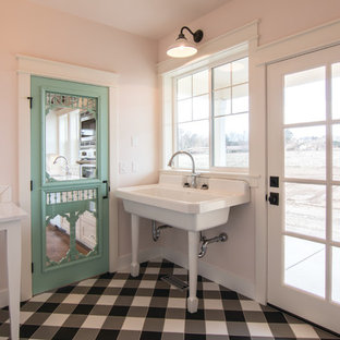 シアトルの小さいカントリー風おしゃれな家事室 (エプロンフロントシンク、ピンクの壁、セラミックタイルの床、左右配置の洗濯機・乾燥機、黒い床) の写真