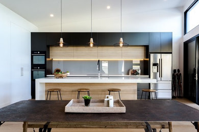 This is an example of a scandinavian galley eat-in kitchen in Adelaide with flat-panel cabinets, grey cabinets, marble benchtops, grey splashback, glass sheet splashback, black appliances, light hardwood floors and with island.