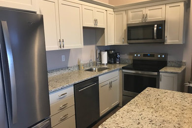Inspiration for a vinyl floor and gray floor kitchen remodel in Milwaukee with a single-bowl sink, shaker cabinets, white cabinets, granite countertops, stainless steel appliances, an island and beige countertops