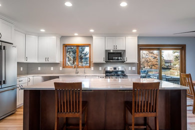 Photo of a mid-sized modern l-shaped eat-in kitchen in Other with an undermount sink, shaker cabinets, white cabinets, quartz benchtops, grey splashback, glass tile splashback, stainless steel appliances, medium hardwood floors, with island and white benchtop.