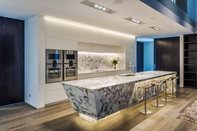 This is an example of a large contemporary single-wall open plan kitchen in Christchurch with an undermount sink, white cabinets, marble benchtops, multi-coloured splashback, marble splashback, medium hardwood floors, with island, brown floor, multi-coloured benchtop, flat-panel cabinets and stainless steel appliances.