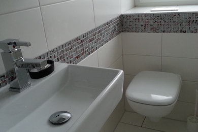 Kleines Modernes Duschbad mit flächenbündigen Schrankfronten, weißen Schränken, Eckbadewanne, Duschbadewanne, Toilette mit Aufsatzspülkasten, weißen Fliesen, weißer Wandfarbe, Aufsatzwaschbecken, weißem Boden und Duschvorhang-Duschabtrennung in Essen