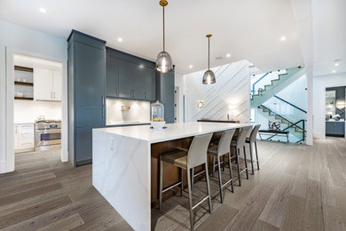 Example of a classic single-wall vinyl floor and brown floor eat-in kitchen design in Los Angeles with a farmhouse sink, flat-panel cabinets, blue cabinets, quartzite countertops, white backsplash, quartz backsplash, stainless steel appliances, an island and white countertops