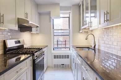 Mid-sized minimalist galley porcelain tile and white floor enclosed kitchen photo in New York with an undermount sink, shaker cabinets, white cabinets, quartzite countertops, white backsplash, subway tile backsplash, stainless steel appliances and black countertops