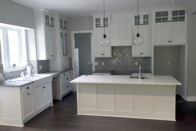 Inspiration for a cottage l-shaped dark wood floor kitchen remodel in Kansas City with a farmhouse sink, shaker cabinets, white cabinets, quartz countertops, gray backsplash and an island