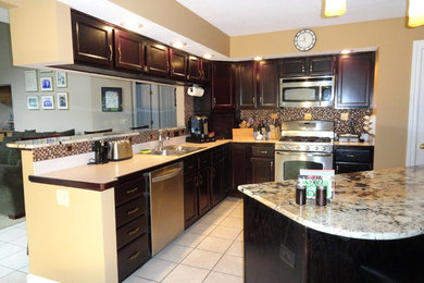 Mid-sized elegant l-shaped ceramic tile and beige floor enclosed kitchen photo in Cleveland with recessed-panel cabinets, dark wood cabinets, an island, a double-bowl sink, granite countertops, multicolored backsplash, mosaic tile backsplash and stainless steel appliances