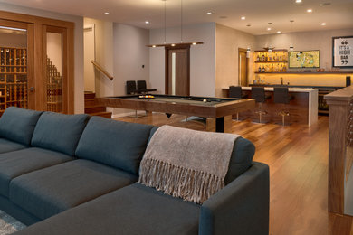 Example of a large minimalist medium tone wood floor and brown floor basement game room design in San Francisco with a bar, a home theater and beige walls
