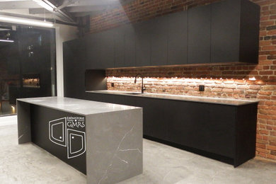 Inspiration for a large modern single-wall concrete floor, gray floor and exposed beam eat-in kitchen remodel in Montreal with an undermount sink, flat-panel cabinets, black cabinets, quartz countertops, red backsplash, brick backsplash, paneled appliances, an island and gray countertops