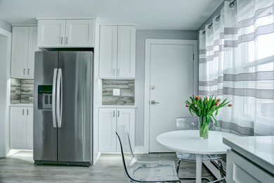 Eat-in kitchen - large contemporary u-shaped vinyl floor and gray floor eat-in kitchen idea in Chicago with an undermount sink, shaker cabinets, white cabinets, quartz countertops, gray backsplash, ceramic backsplash, stainless steel appliances, no island and white countertops