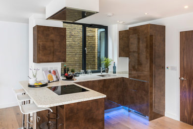 Contemporary u-shaped kitchen in London with a submerged sink, flat-panel cabinets, brown cabinets, light hardwood flooring, a breakfast bar, brown floors and beige worktops.
