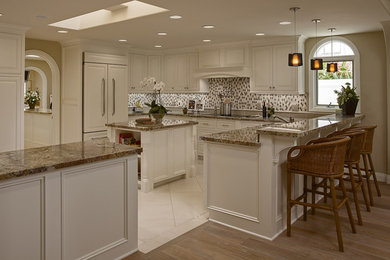 Inspiration for a large coastal u-shaped limestone floor eat-in kitchen remodel in Orange County with an undermount sink, raised-panel cabinets, white cabinets, granite countertops, multicolored backsplash, glass tile backsplash, stainless steel appliances and an island