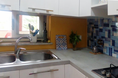 Photo of a small modern l-shaped open plan kitchen in Other with a built-in sink, flat-panel cabinets, white cabinets, laminate countertops, orange splashback, porcelain splashback, stainless steel appliances, porcelain flooring, grey floors and grey worktops.
